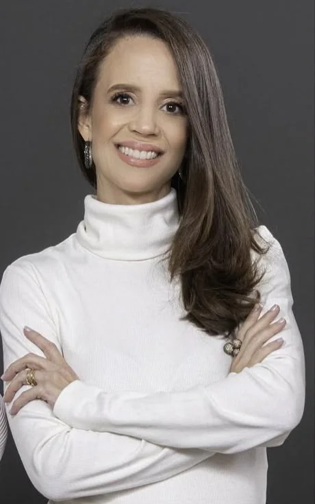 Lívia Ribeiro, da liderança da Automatize Projetos: cabelo castanho longo, blusa branca de gola alta, braços cruzados